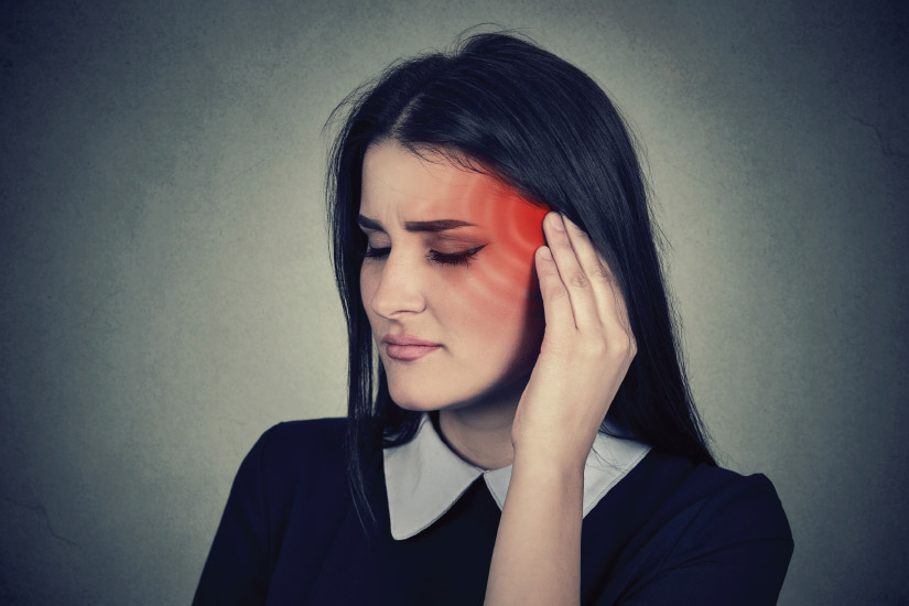 Woman holding the side of her head near her ear, illustrating symptoms associated with tinnitus and ear discomfort.